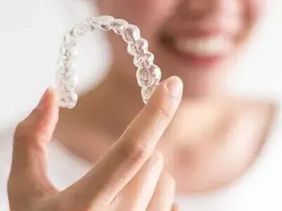 Dental Alignment through Orthodontics Wimbledon - A patient at Ridgway Dental, a dental clinic in Wimbledon is holding a clear dental aligner, highlighting the advanced orthodontic treatments offered by the clinic. The patient is smiling, indicating satisfaction with the comfortable and nearly invisible aligner. This scene underscores Ridgway Dental's commitment to providing modern and effective solutions for dental alignment, ensuring improved oral health and enhanced aesthetics.