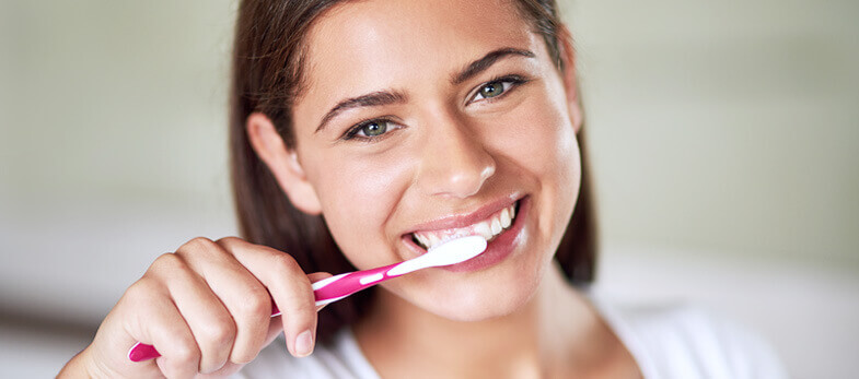 dental hygienist wimbledon - A woman with a radiant smile is pictured brushing her teeth with a pink toothbrush, symbolizing proper oral hygiene practices promoted at Ridgway Dental, a dental clinic in Wimbledon. The setting appears to be a well-lit, welcoming room, possibly within the dental office. This image serves as a cheerful reminder of the importance of daily dental care and the professional dental hygiene services offered by Ridgway Dental to maintain a healthy, vibrant smile.