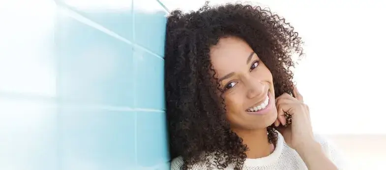 Orthodontics Wimbledon - A young woman smiles brightly, displaying her perfectly aligned teeth, a testament to the orthodontic treatment she received at Ridgway Dental, a dental clinic in Wimbledon. Leaning against a light blue tiled wall, her joyful expression reflects the confidence gained from her straightened teeth. This image highlights the successful results of orthodontic care provided by Ridgway Dental, emphasizing their expertise in creating beautiful, healthy smiles through advanced orthodontic techniques.