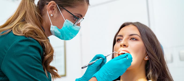 Periodontist Wimbledon - A patient is undergoing a dental examination at Ridgway Dental, a dental clinic in Wimbledon. The periodontist, equipped with a mask and gloves, is using dental instruments to carefully examine the patient's teeth and gums. The clinical setting is clean and modern, indicating a professional and hygienic environment. The patient is seated comfortably in the dental chair, reflecting the clinic's focus on providing a relaxed and stress-free experience. This scene showcases Ridgway Dental's dedication to thorough periodontal care and the well-being of their patients in Wimbledon.